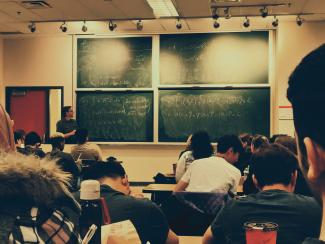 student sitting on chairs in front of chalkboard by Shubham Sharan courtesy of Unsplash.